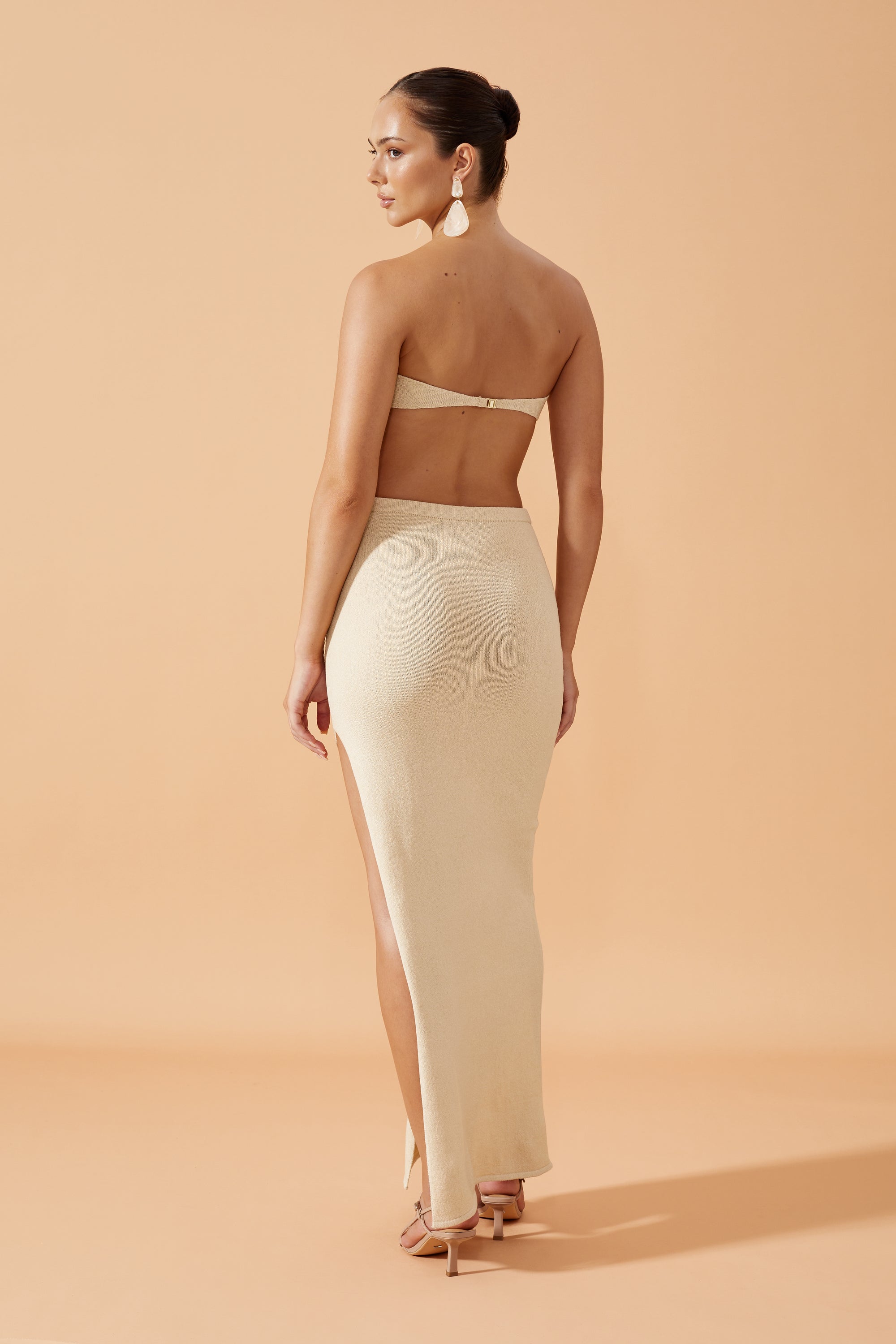 Flook The Label Chika Knit Long Skirt with side slit in Sand,  worn with drop resin earrings, back view